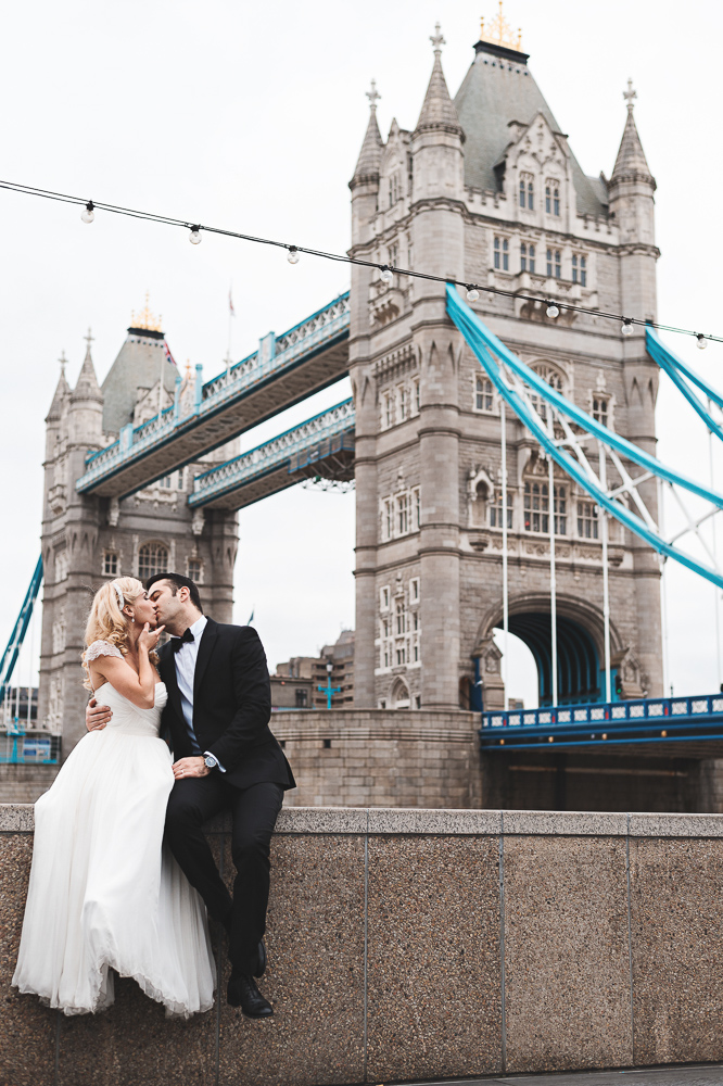 Bride and groom kissing in front of a London Bridge - The Now Time