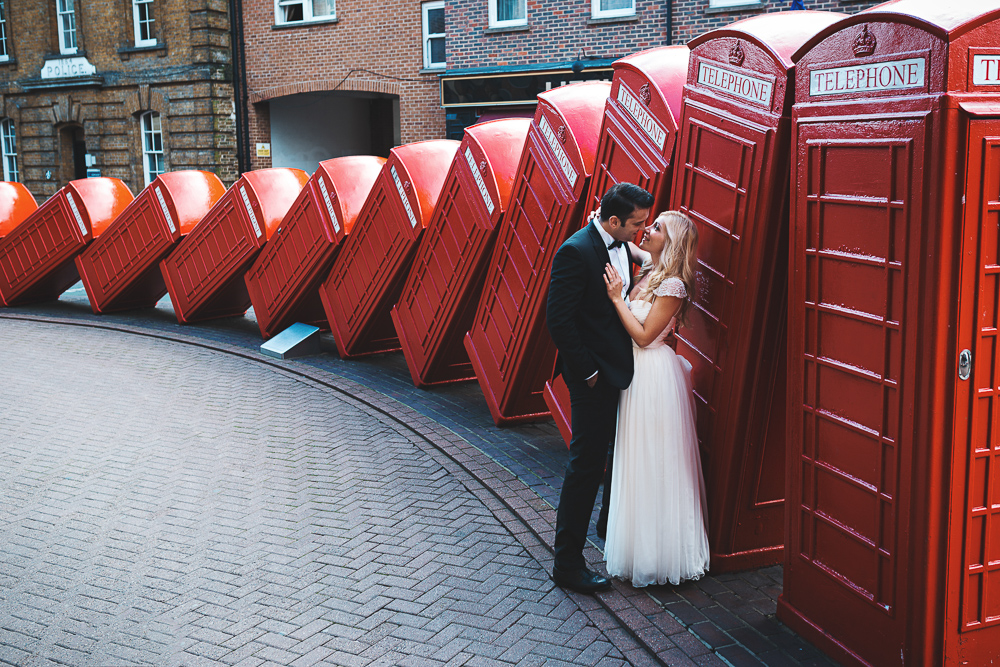 Bride and groom posing for wedding photos against red telephone boots in one of the best London photo shoot locations