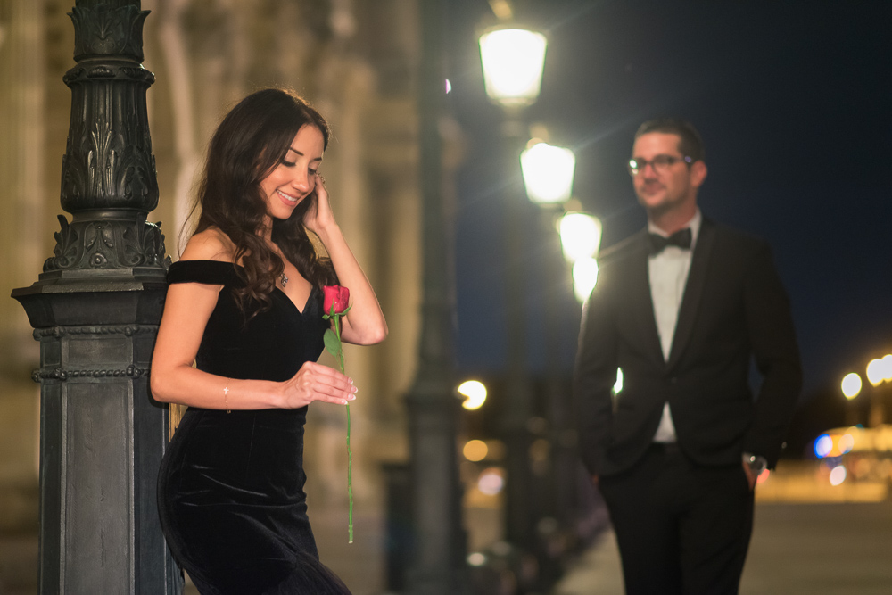 Woman in black dress holding a red rose as a prop during her engagement photos in the city of lights