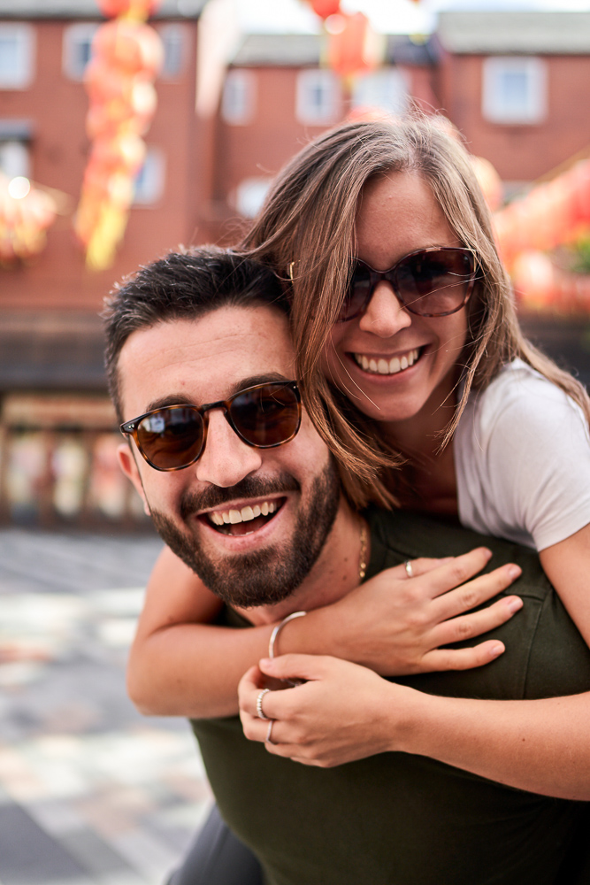 Girl on man's back looking into camera and smiling during engagement photosession