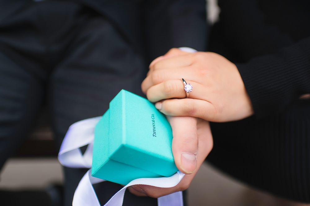 Newly engaged couple holding hands with Tiffany & Co engagement ring box