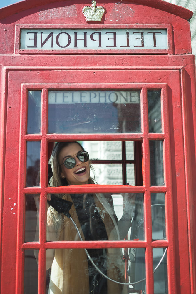 Young girl smiling from a red telephone boot in London while posing for professional photos