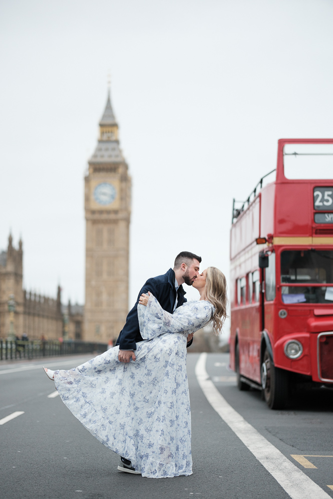 Couple kissing in the middle of the street next to a red bus and in front of Big Ben