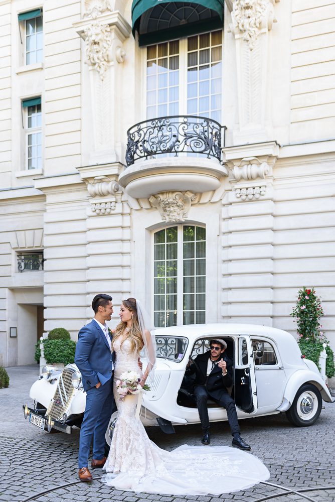 Bride and groom posing for photos next to a vintage car