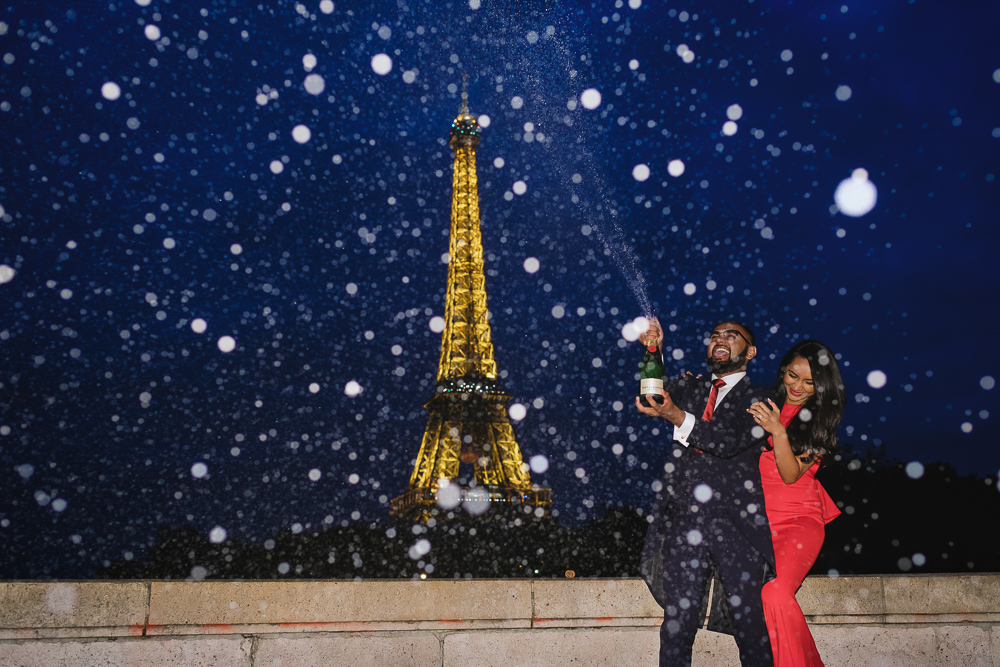 Couple popping champagne in Paris at night during their engagement photoshoot