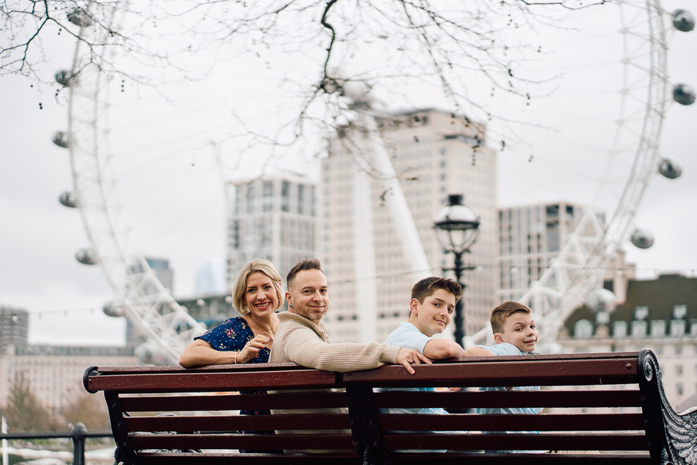 Family of tourists sitting on a bench and posing for professional photos on south bank overlooking the London Eye