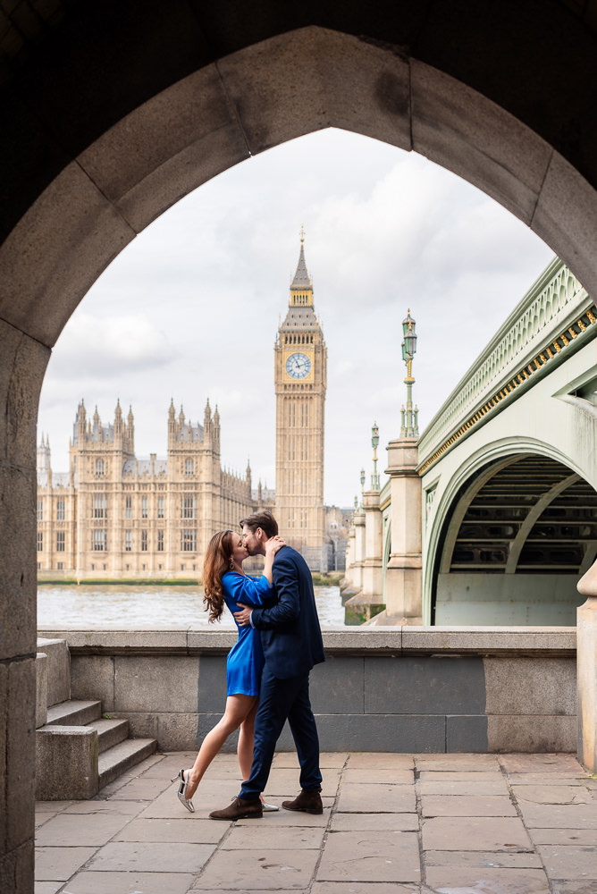 Couple kissing under the Westminster bridge overlooking Big Ben during London engagement photoshoot