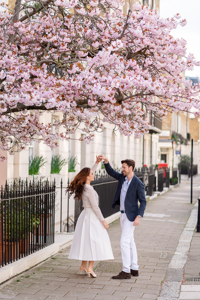 Newly engaged couple dancing under a cherry blossom in Chelsea London during engagement photoshoot