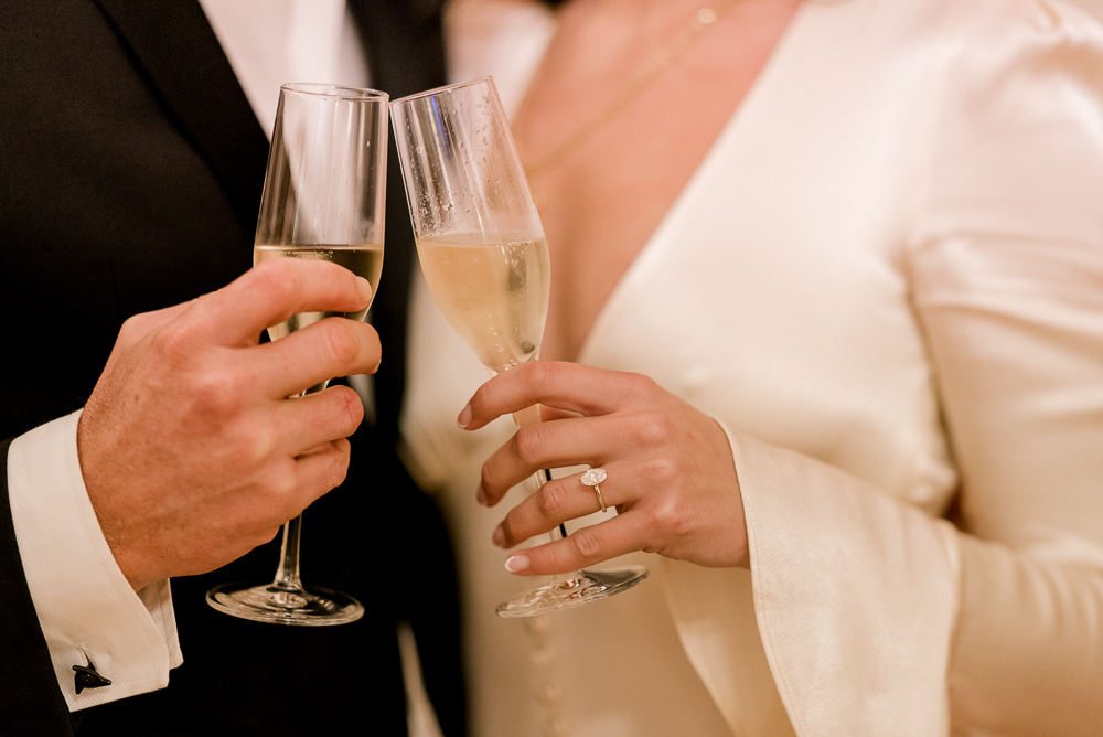 Close up on hands holding glasses with champagne and woman wearing new engagement ring