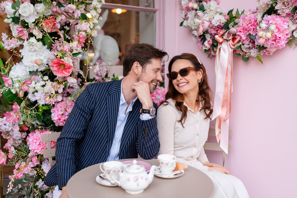 Couple posing for engagement photos in a café surrounded by pink flowers