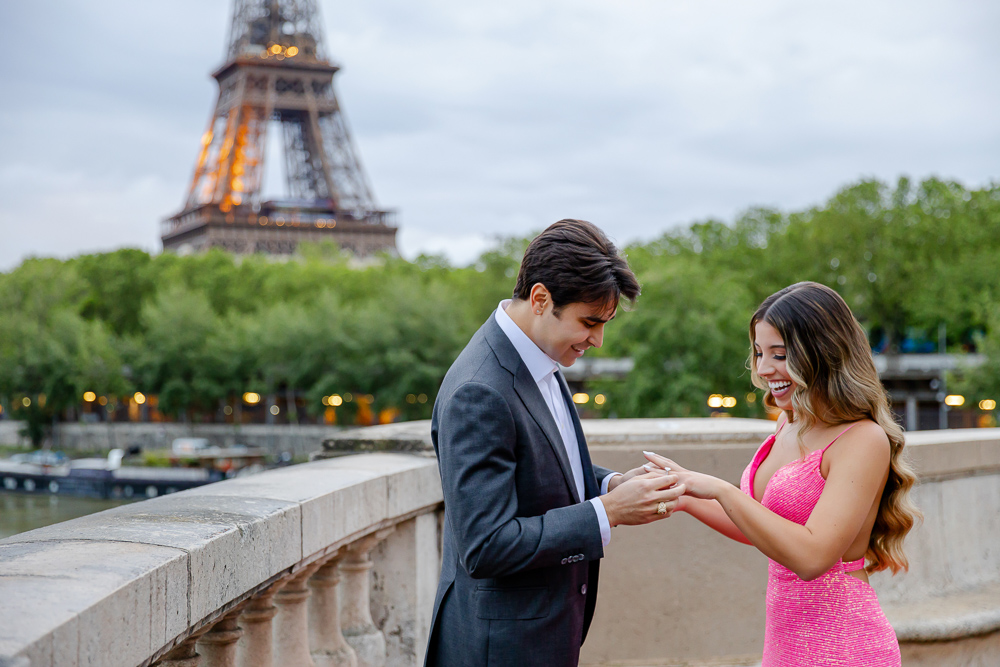 Woman smiling happily while man puts on diamond ring on her finger
