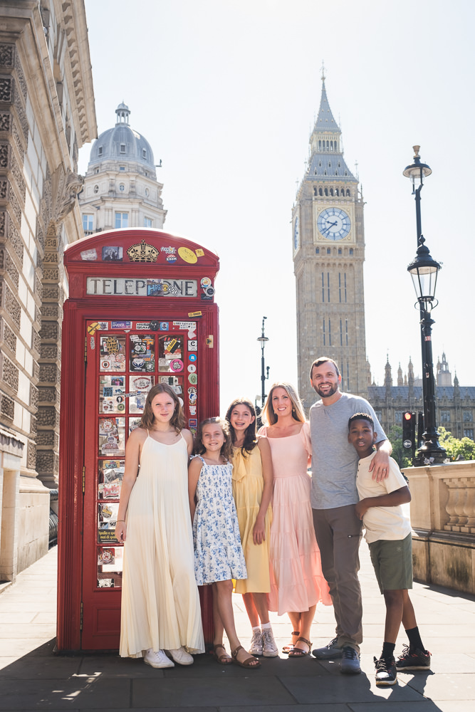 Happy family posing for family portraits by a red telephone boot overlooking Big Ben