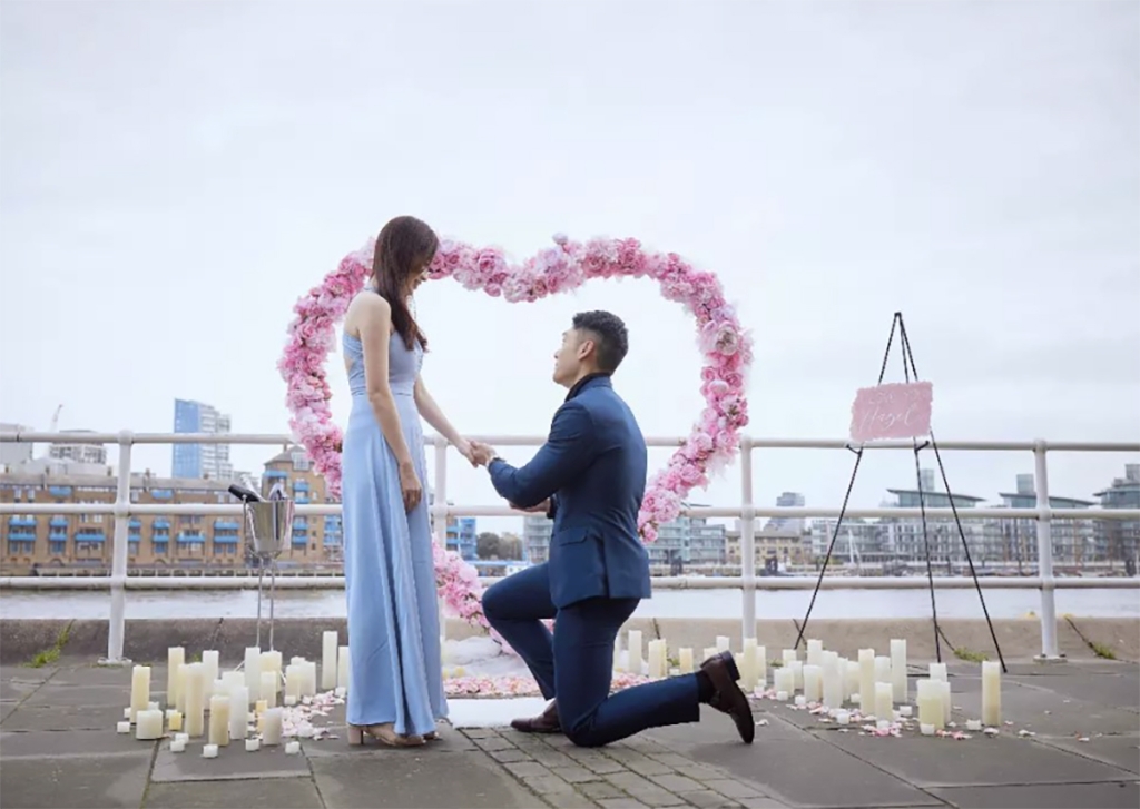 Man proposing to his future fiancée in front of pink heart made of flowers