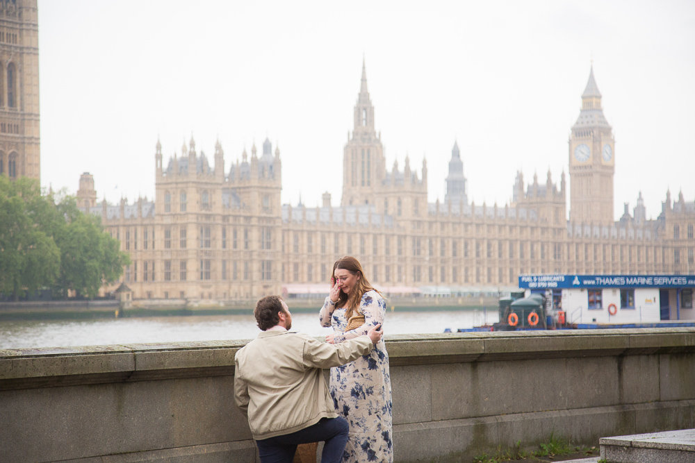 Man on his knee proposing to his girlfriend in the rain in London by Westminster Abbey