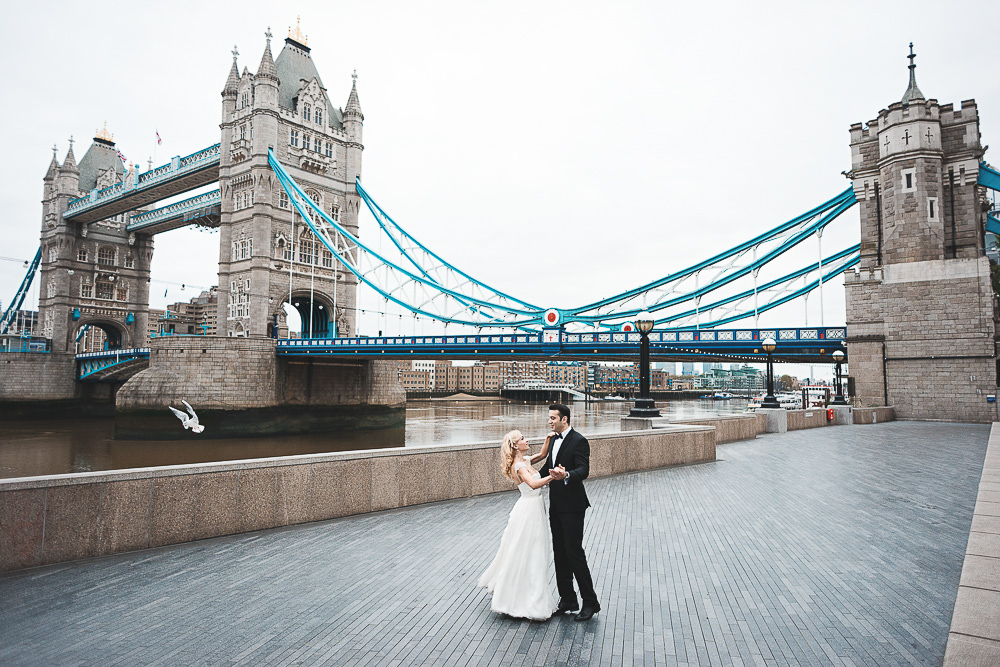 Bridge and groom posing for wedding photos on Queen's Walk at Tower Bridge in London