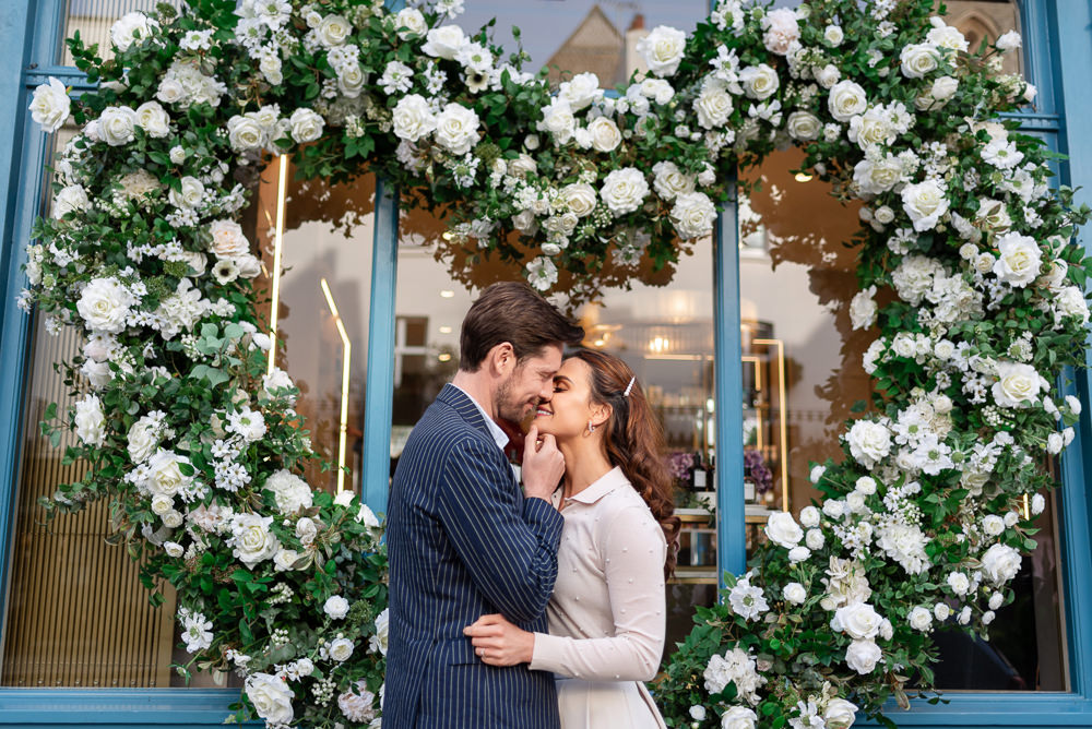 Romantic couple kissing in front of heart shaped storefront made of white flowers